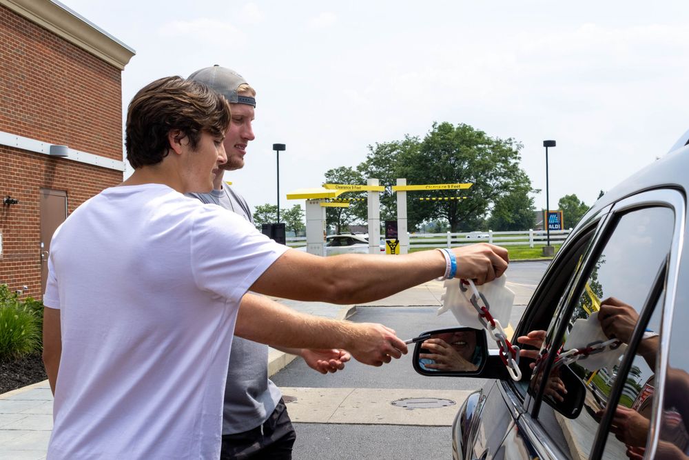 Two young men hand items to a customer through a car window at a McDonald's drive-thru.