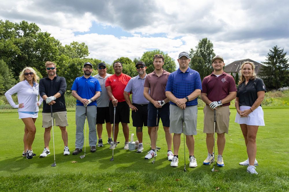 Group of ten golfers posing together on a green golf course under a cloudy sky.