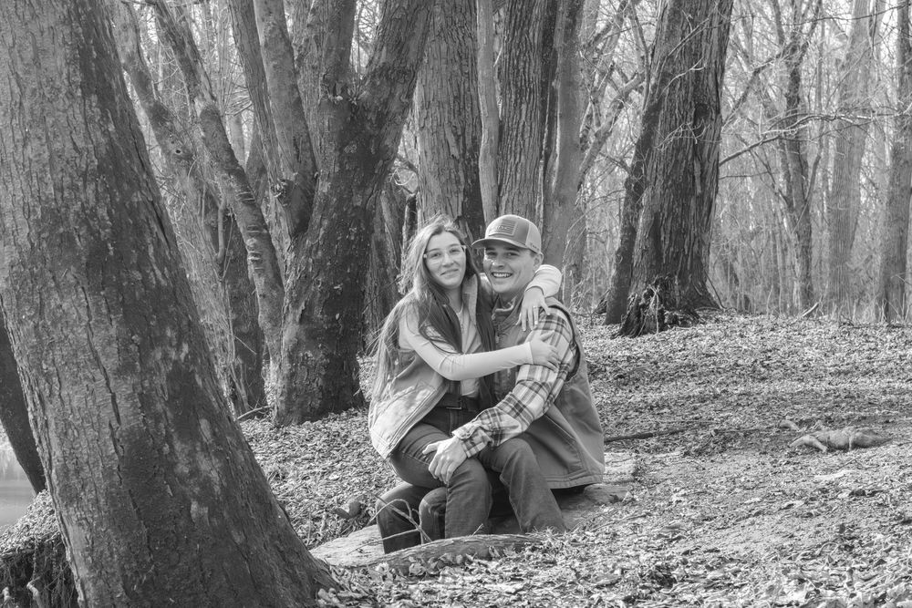 Black and white photo of couple sitting together among trees in autumn forest.