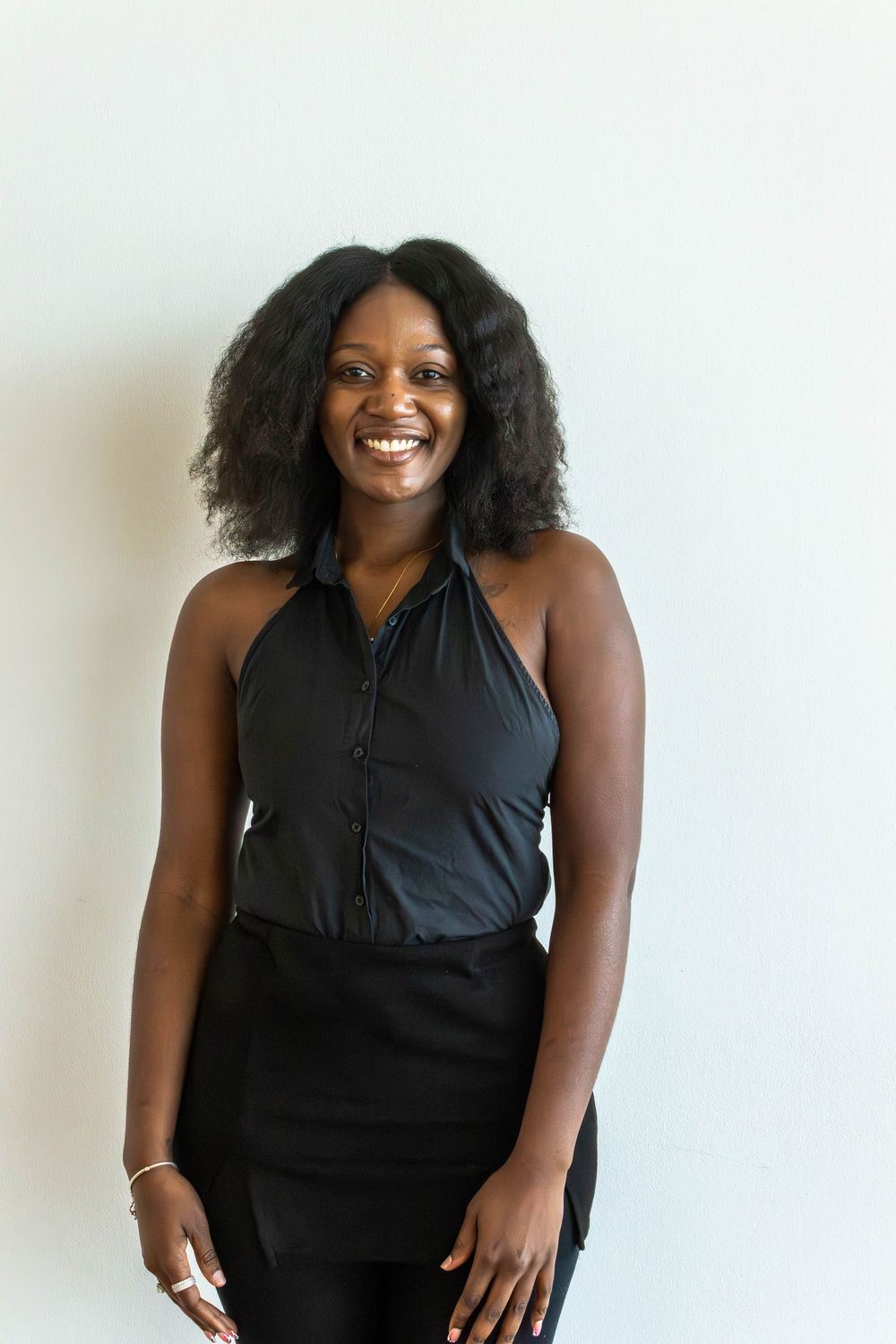 Smiling young woman in black halter top posing against white wall.