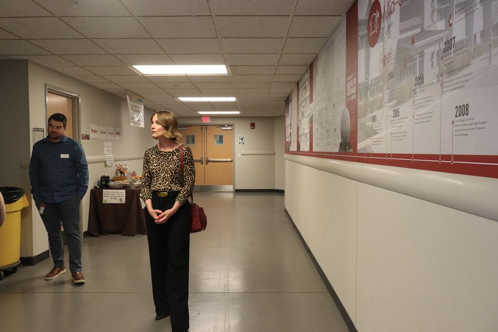 Woman in leopard print top standing in a hallway with historical timeline displayed on red wall.