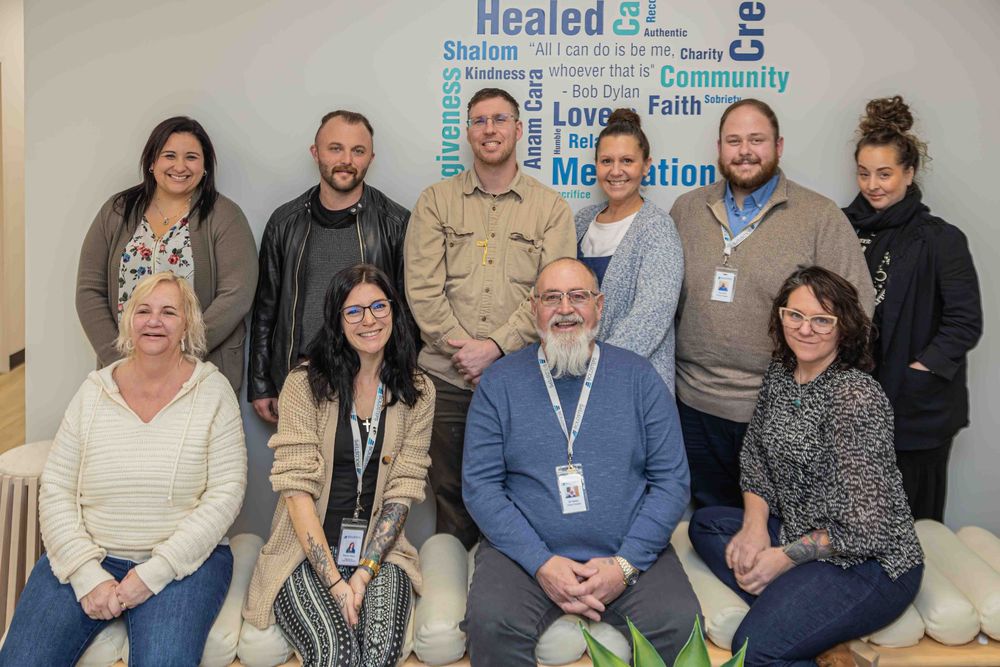 Group of ten diverse professionals posing together in a modern office with an inspirational word wall.