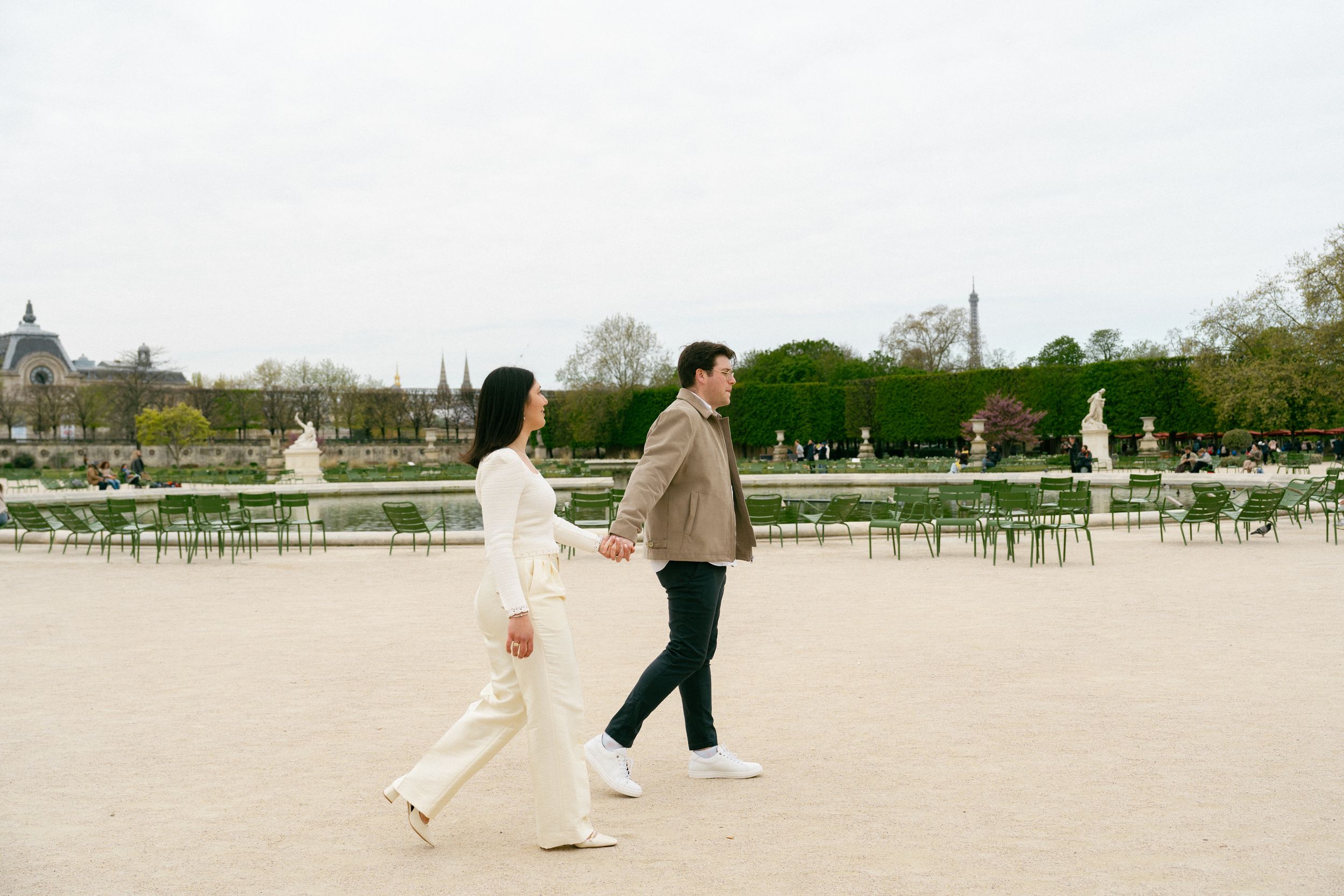 Couple holding hands walking through Tuileries Garden in Paris with the Eiffel Tower in the background. Paris editorial photographer