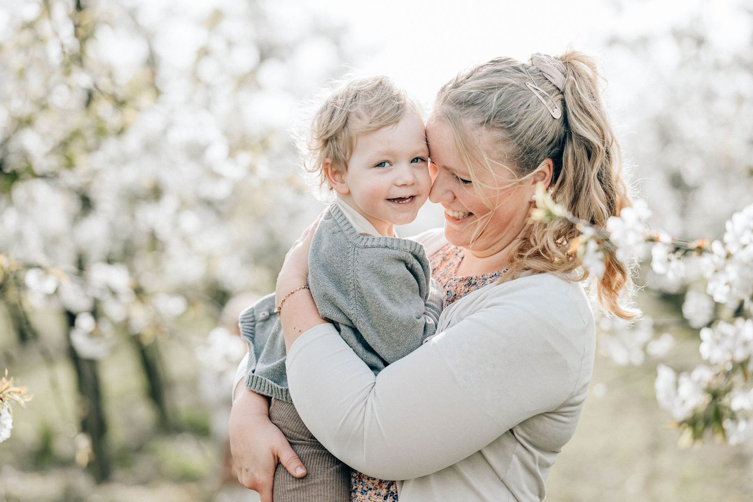 Eine glückliche Mutter hält ihr Kind in den Armen in der Kirschblüte des Alten Landes beim Fotoshooting mit Julia Aßmann Fotografie.