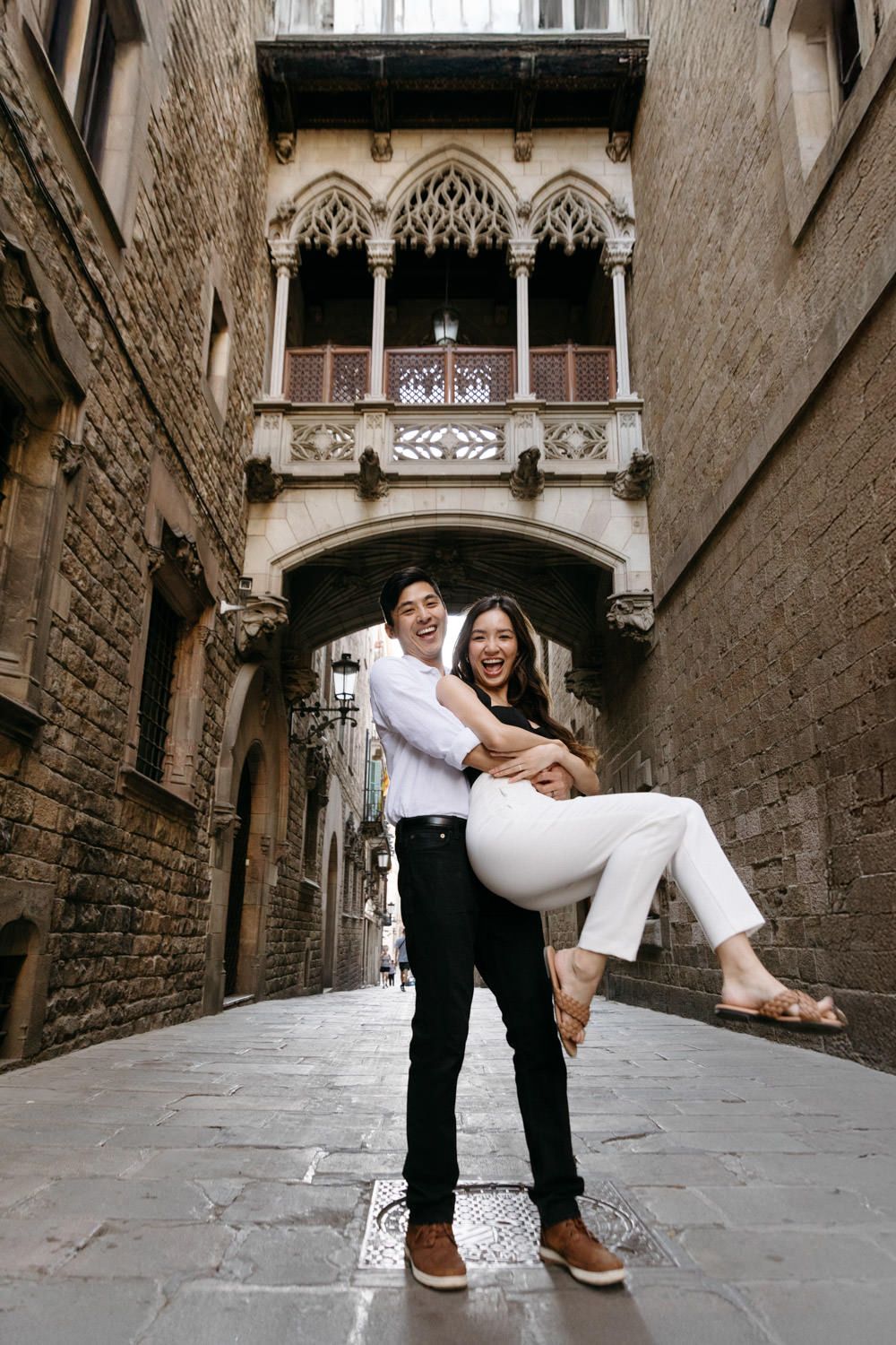 Playful couple poses in Gothic Quarter alleyway with historic stone architecture.