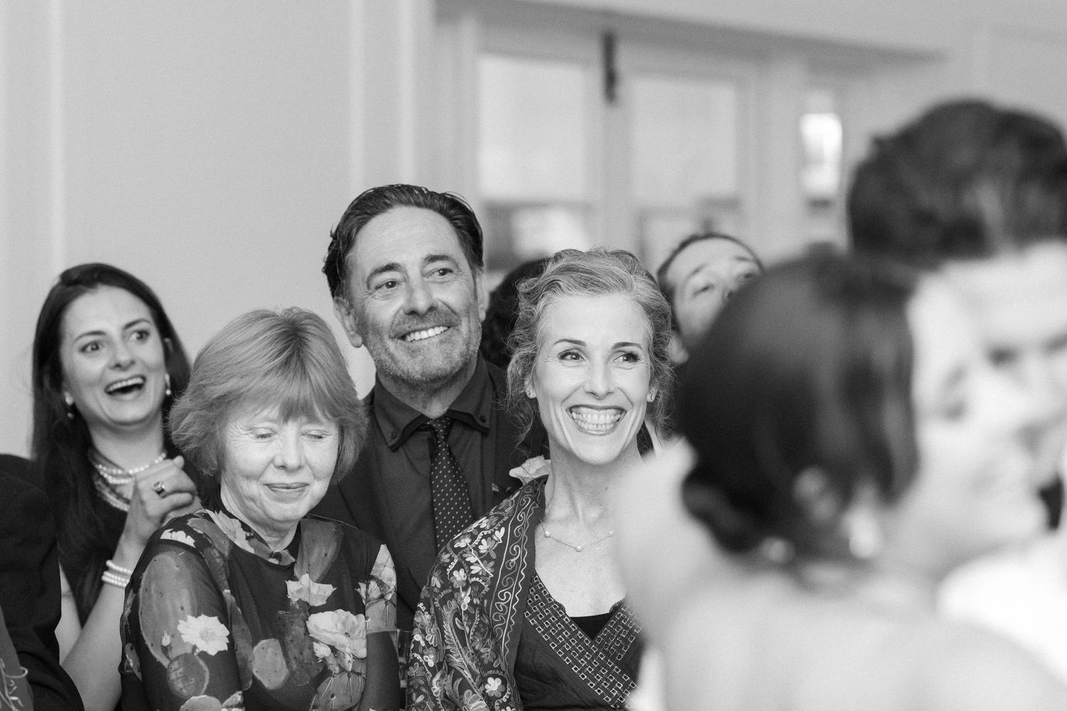 Black and white photograph of guests sharing smiles and laughter at a wedding celebration.