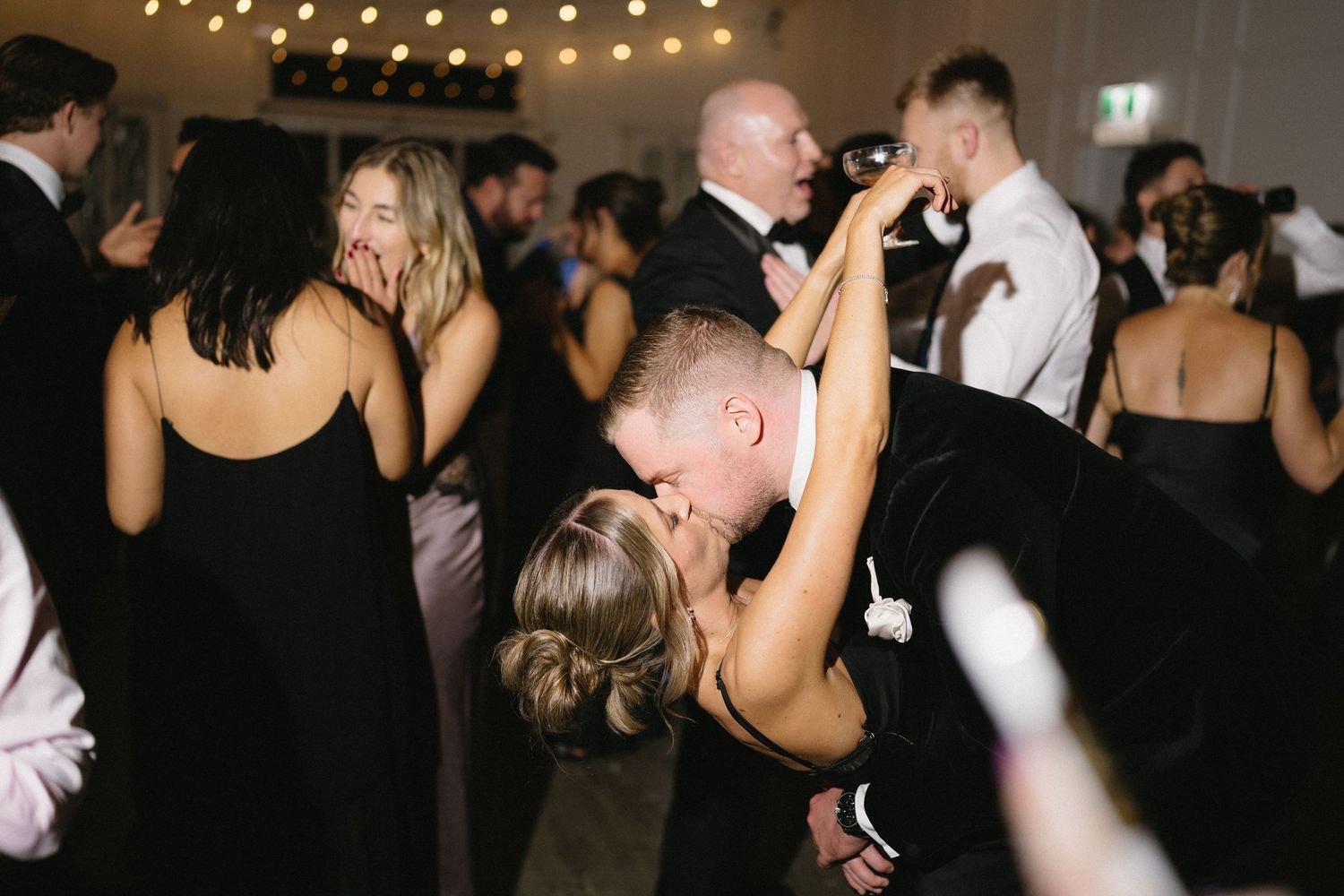 Wedding guests dancing energetically under string lights at an evening reception.
