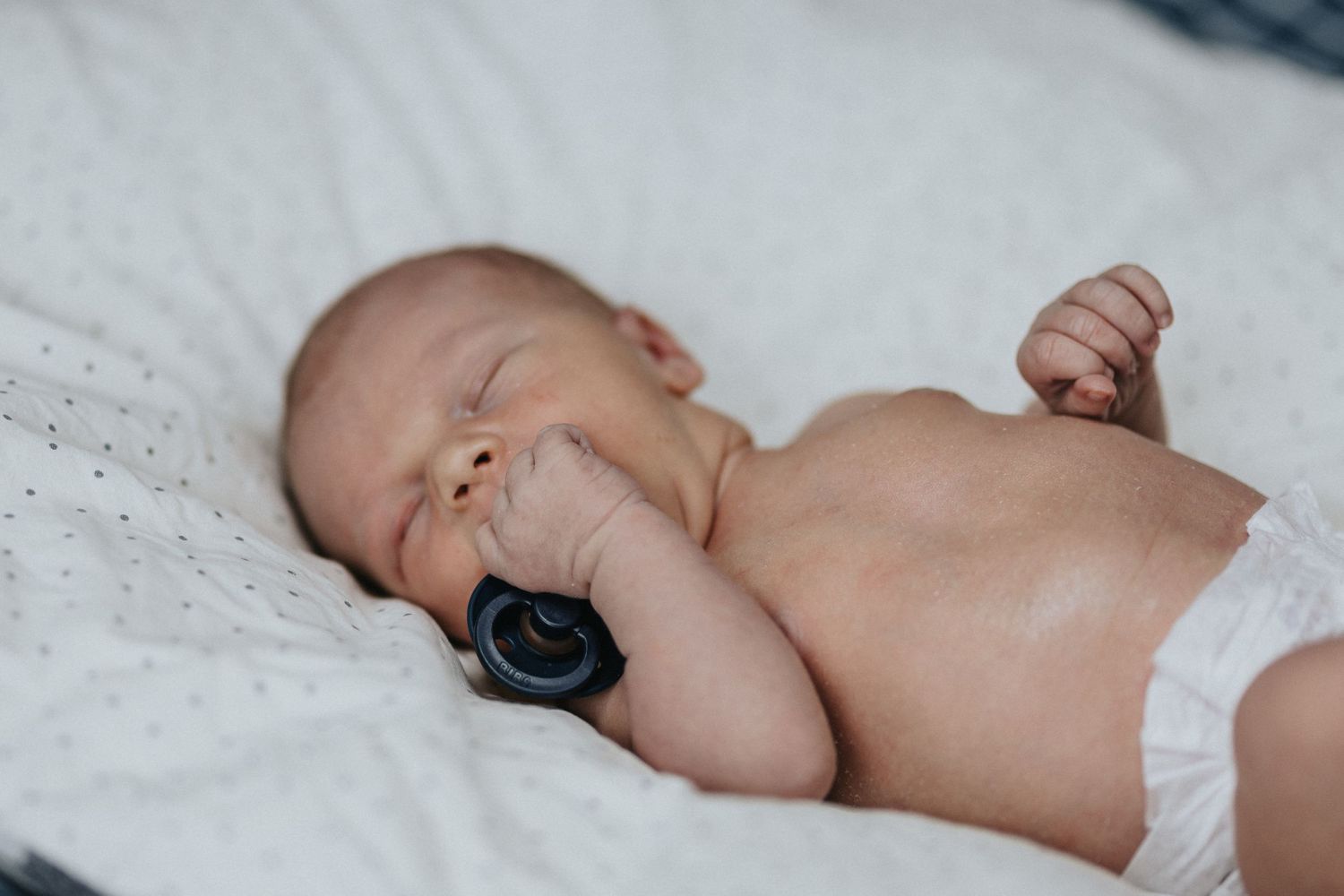 Sleeping newborn baby in white diaper rests peacefully on white bedding.
