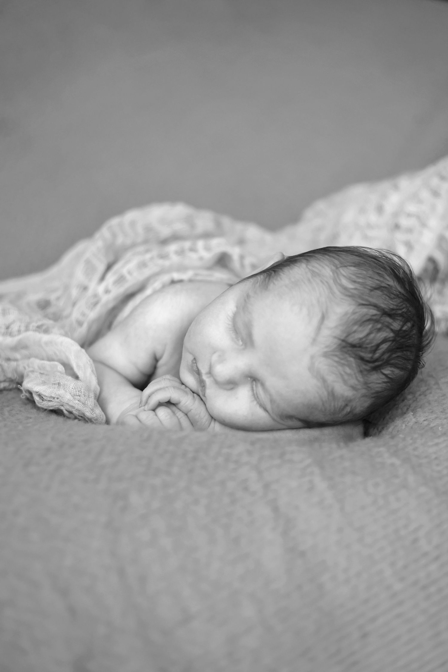 Newborn baby sleeping peacefully on textured blanket in black and white.