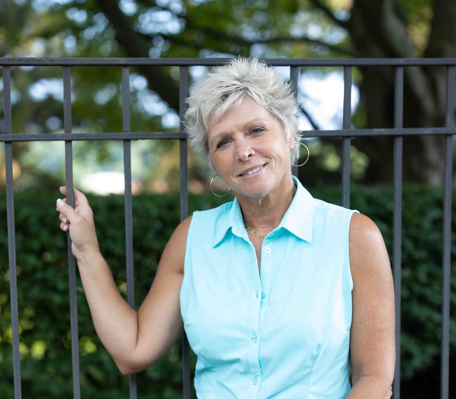 Outdoor portrait in aqua sleeveless blouse leaning against metal railing.