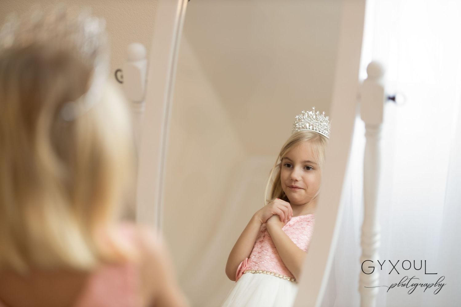 Reflection in mirror shows young person wearing tiara and pink dress.