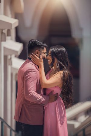 Romantic moment between couple wearing coordinated pink outfits in archway setting.