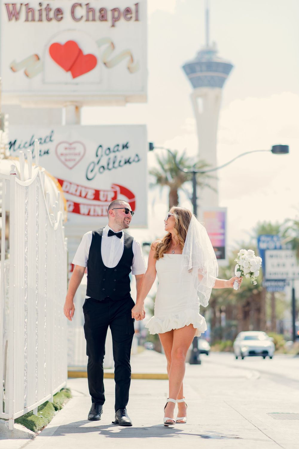 A couple poses outside the iconic White Chapel in Las Vegas with the Stratosphere tower visible in the background.