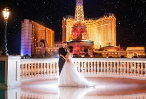 A couple shares a romantic moment on an illuminated balcony overlooking the glittering Las Vegas strip at night.