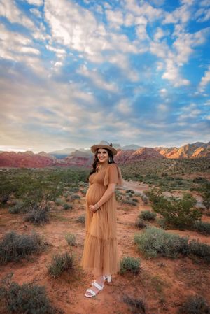 A maternity photo shoot in a desert landscape with red rocks and dramatic clouds.