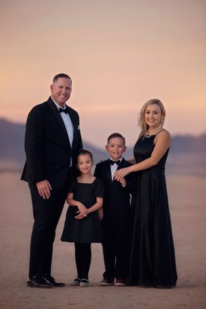 A formal family portrait at sunset on a beach wearing elegant black attire.