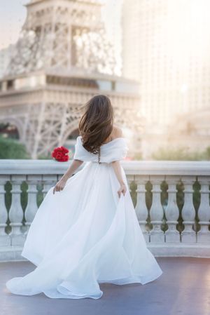 An elegant white wedding dress flowing in the breeze with the Eiffel Tower visible in the background.