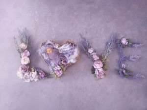 The word 'LOVE' spelled out with delicate purple and pink dried flowers and foliage on a gray background.
