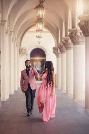 Couple in matching pink outfits walking through elegant arched colonnade.