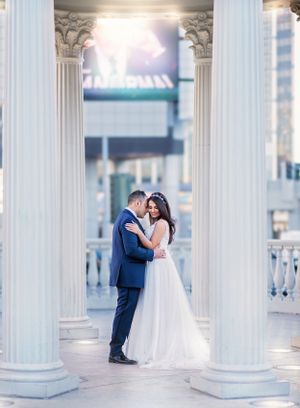 A romantic wedding moment captured between classic white columns with soft natural lighting.