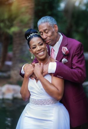 A tender wedding portrait moment with a burgundy suit and white dress against a natural backdrop.