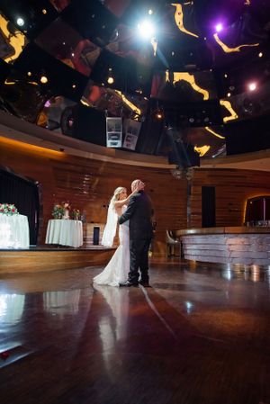 A wedding couple shares their first dance in a rustic venue with dramatic ceiling lighting.
