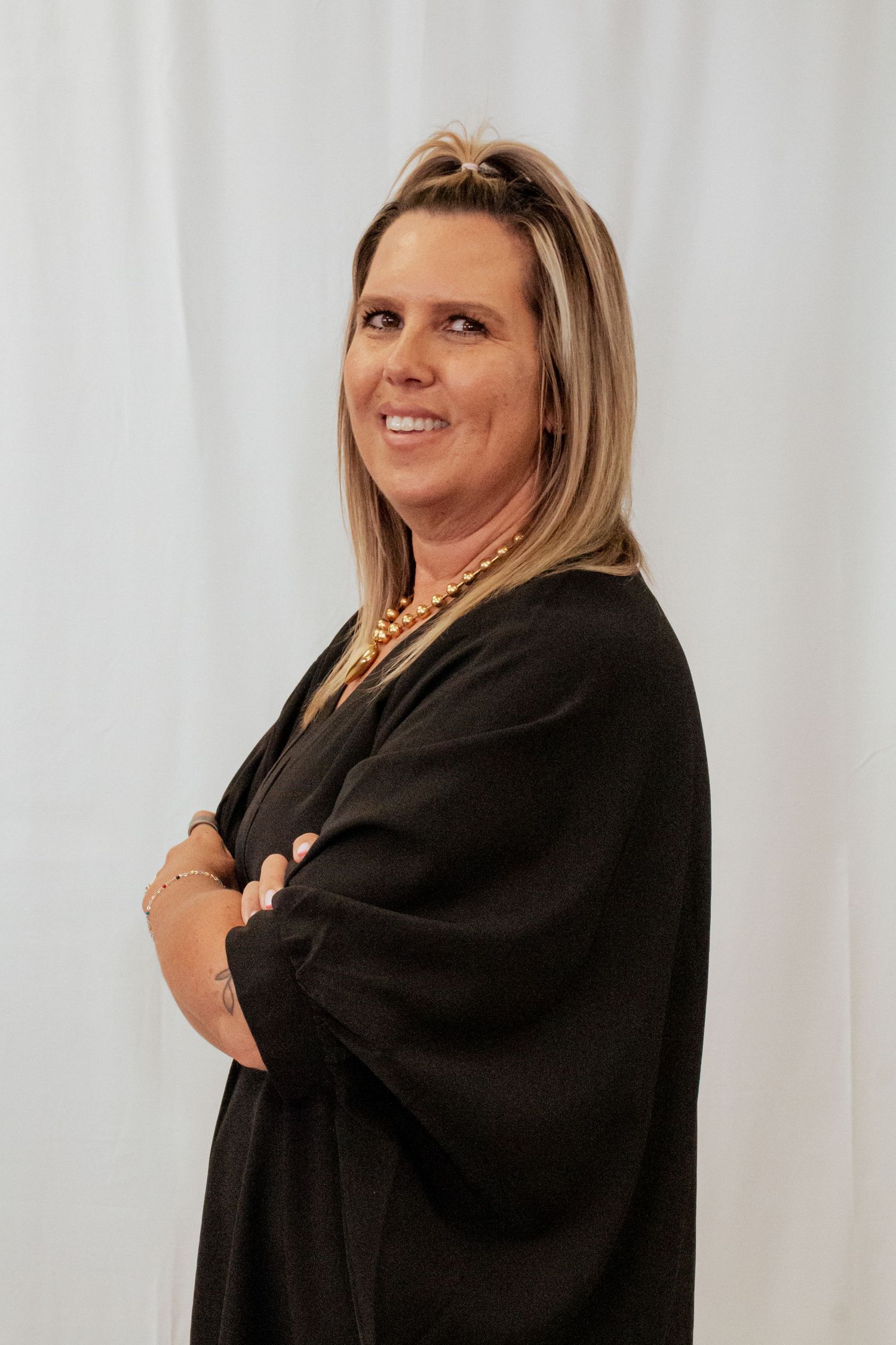 Professional business portrait of a person in a black blazer smiling with crossed arms against a white backdrop.