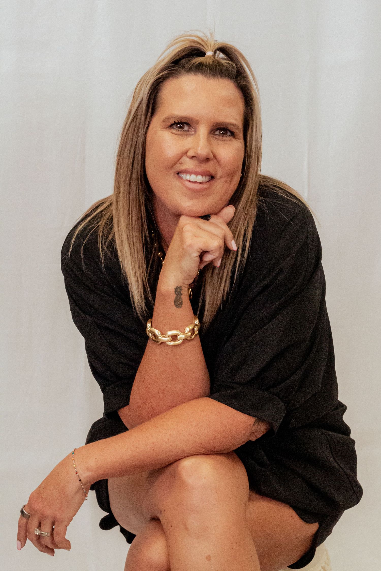 A person in a black button-down shirt poses with a warm smile while sitting against a light background.