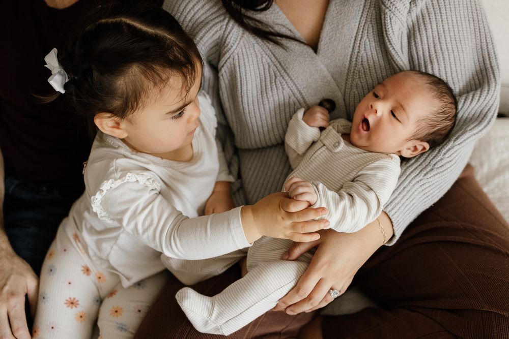 Lifestyle newborn photography in San Jose features baby in his mother's arms while his sibling holds his hand