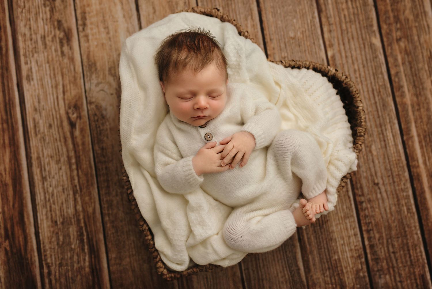 Charlottesville newborn photographer captures a baby boy as he cozies up on white knit blankets in a heart basket against a warm wood floor.