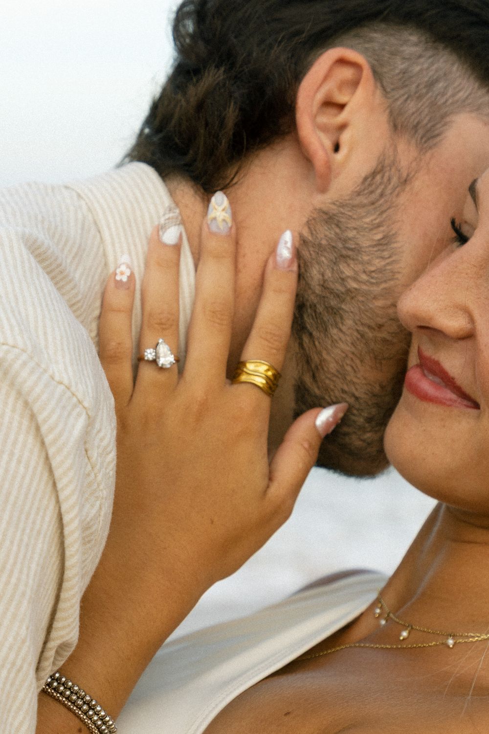 Close-up of couple embracing, woman showing diamond engagement ring and gold band on manicured nails.