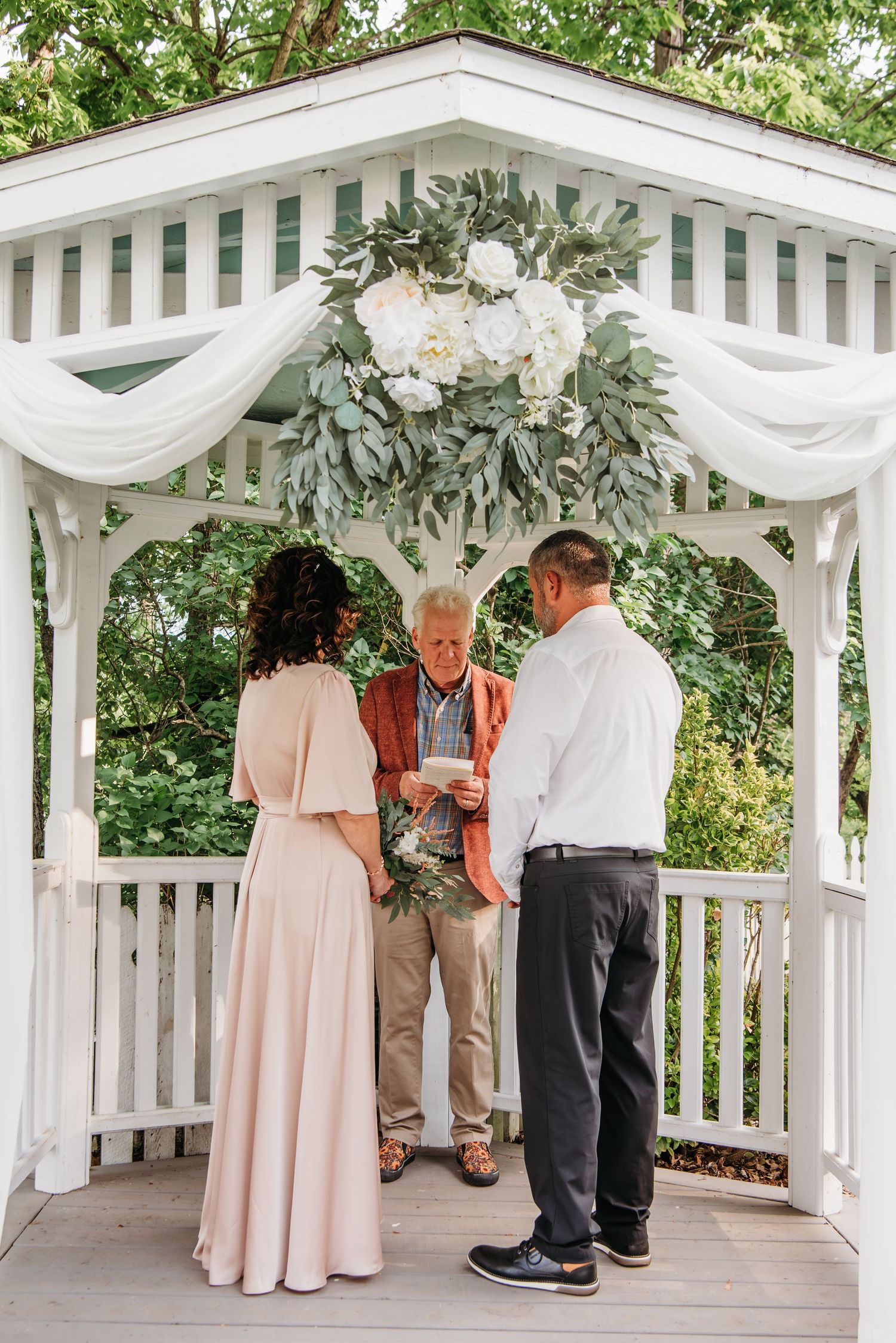 Wedding ceremony setup in a white gazebo decorated with floral arrangements and fabric draping at the Appalachian Wedding Chapel.