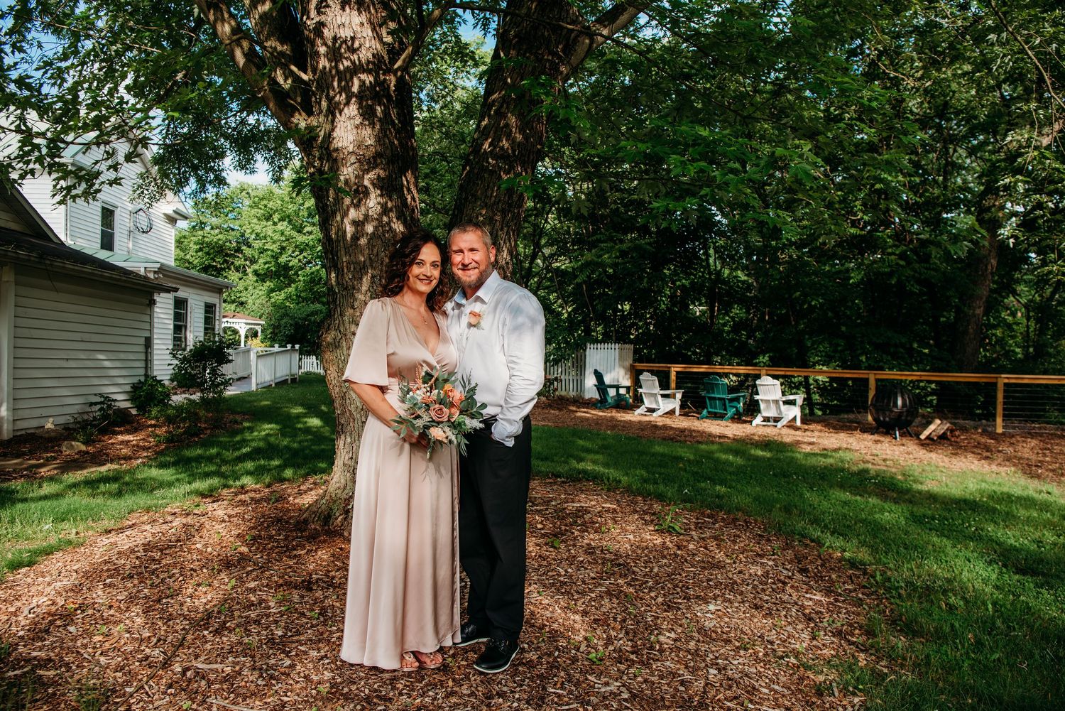 A couple embracing on grass-covered grounds with trees in the background at the Appalachian Wedding Chapel.