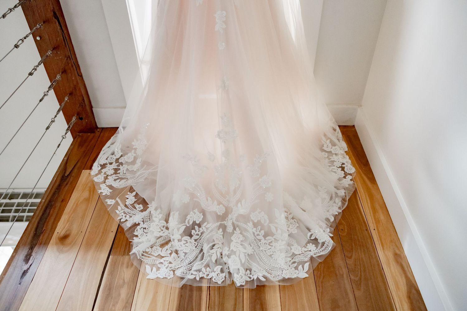 Intricate lace detail on the hem of a flowing white wedding dress train draped over hardwood flooring.