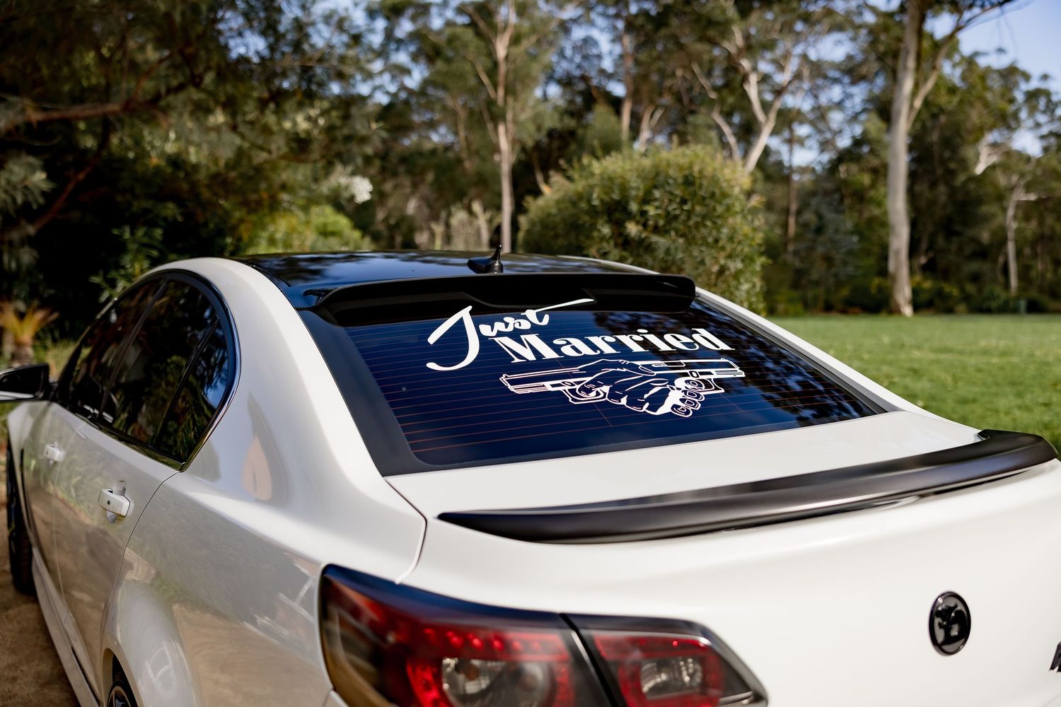 White car with Just Married decal and heart design on rear window parked in outdoor nature setting.