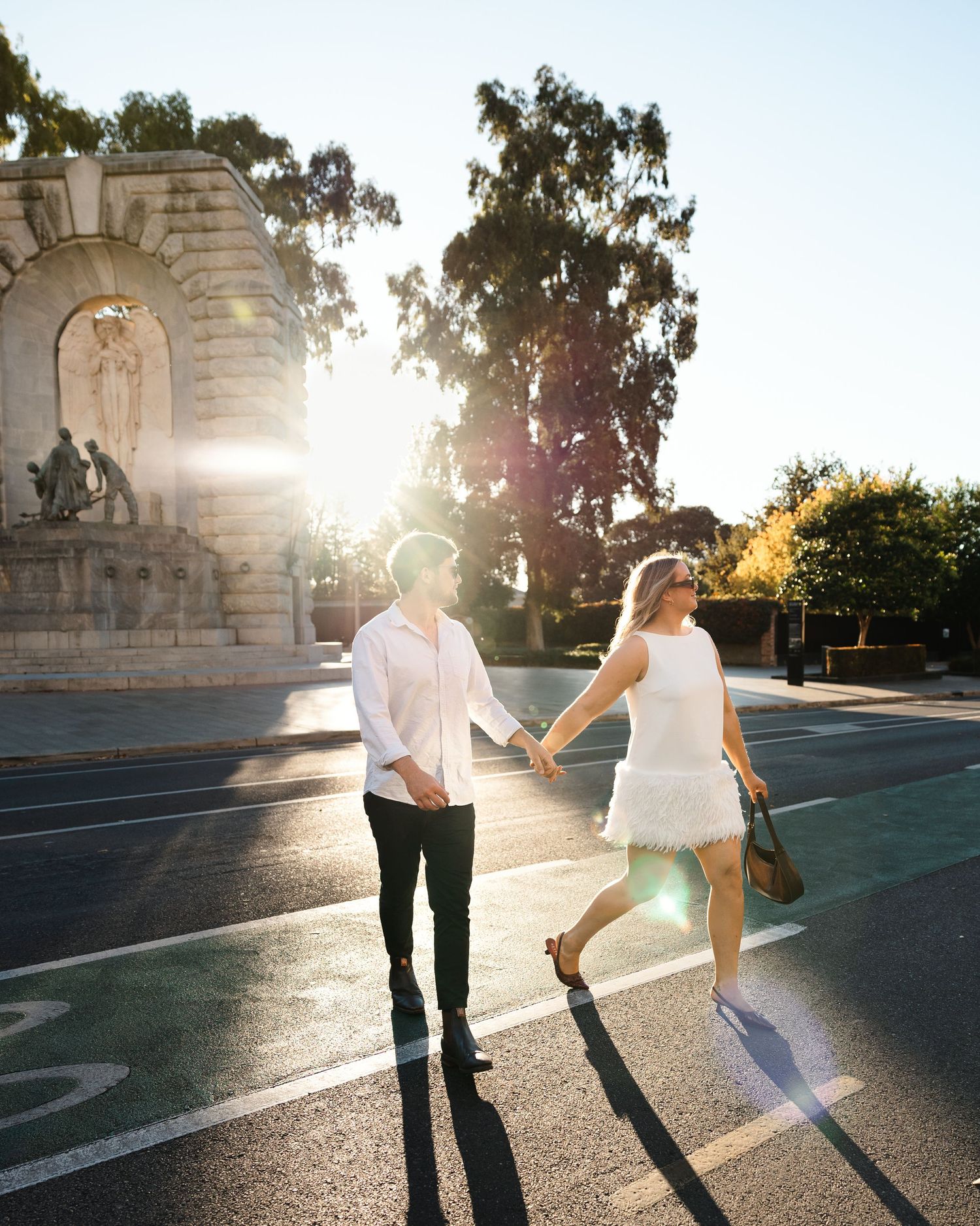 Stylish couple in monochromatic outfits walking hand in hand along a historic colonnade with stone architecture.