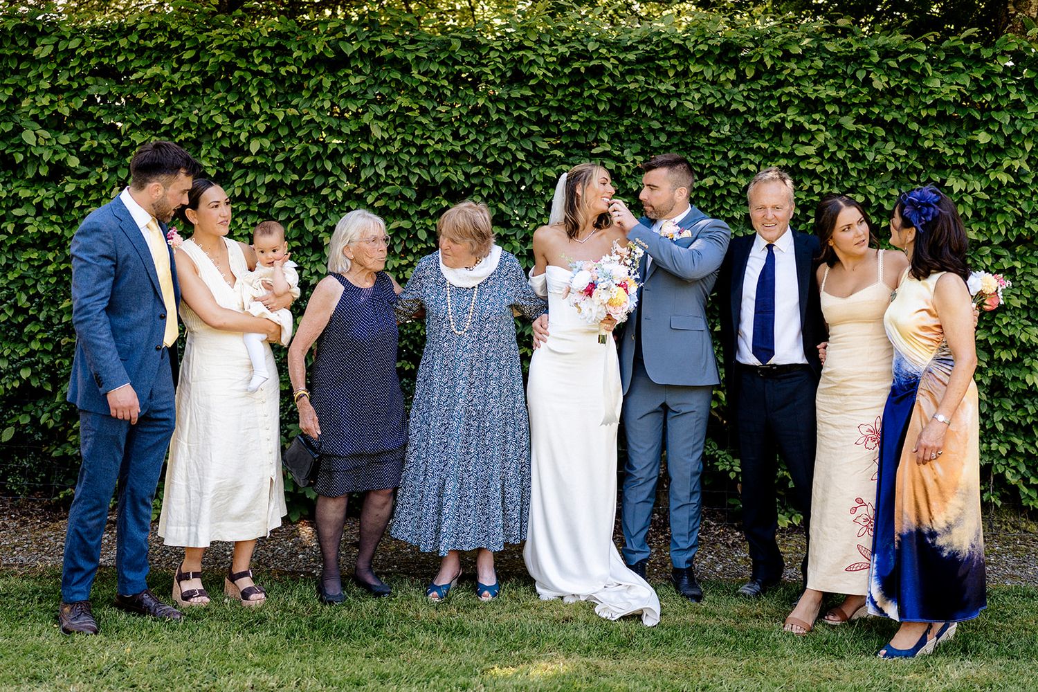A joyful wedding party standing in a line against an ivy-covered wall backdrop in a garden setting.
