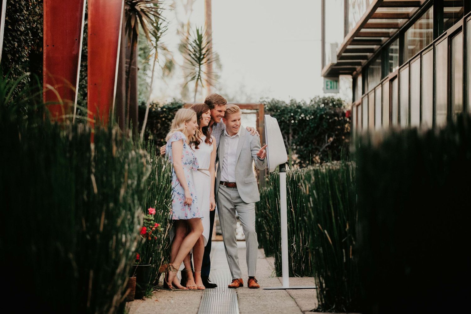 A couple stands together on a pathway between buildings surrounded by lush greenery and palm trees at dusk.