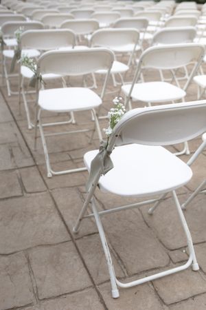 Rows of white folding chairs arranged on a stone patio for an outdoor event.