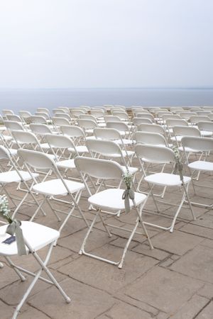 White folding chairs set up in neat rows against an ocean backdrop for a seaside ceremony.