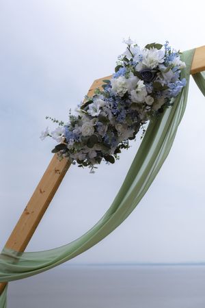 Elegant floral arch decoration with white and blue flowers against a cloudy sky.