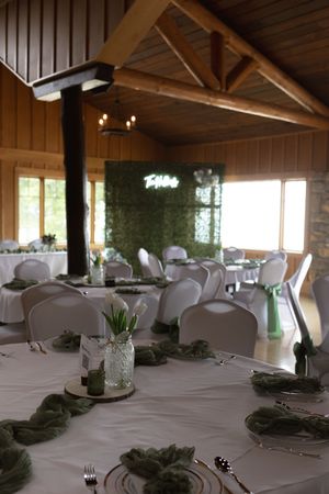 Rustic wooden reception venue with white tablecloths and natural greenery decorations.