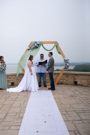 A wedding ceremony in progress under a wooden hexagonal arch with floral decorations on a scenic overlook.