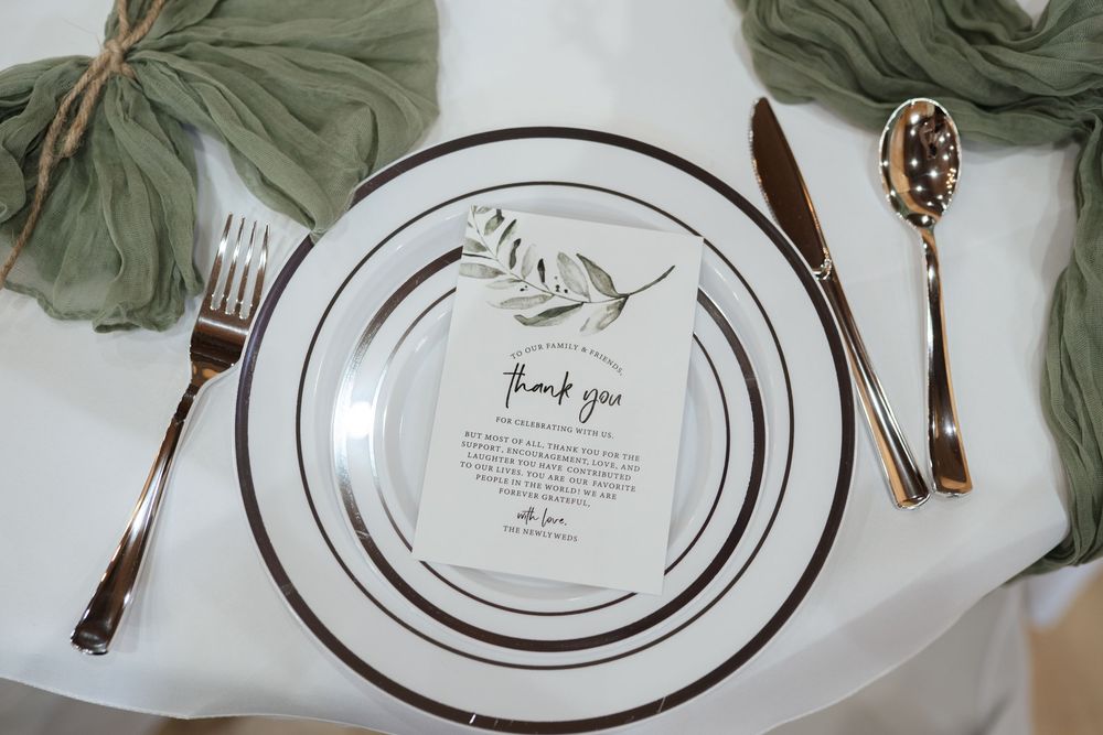 Elegant place setting with white plates, silver utensils, and sage green accents featuring a thank you note.