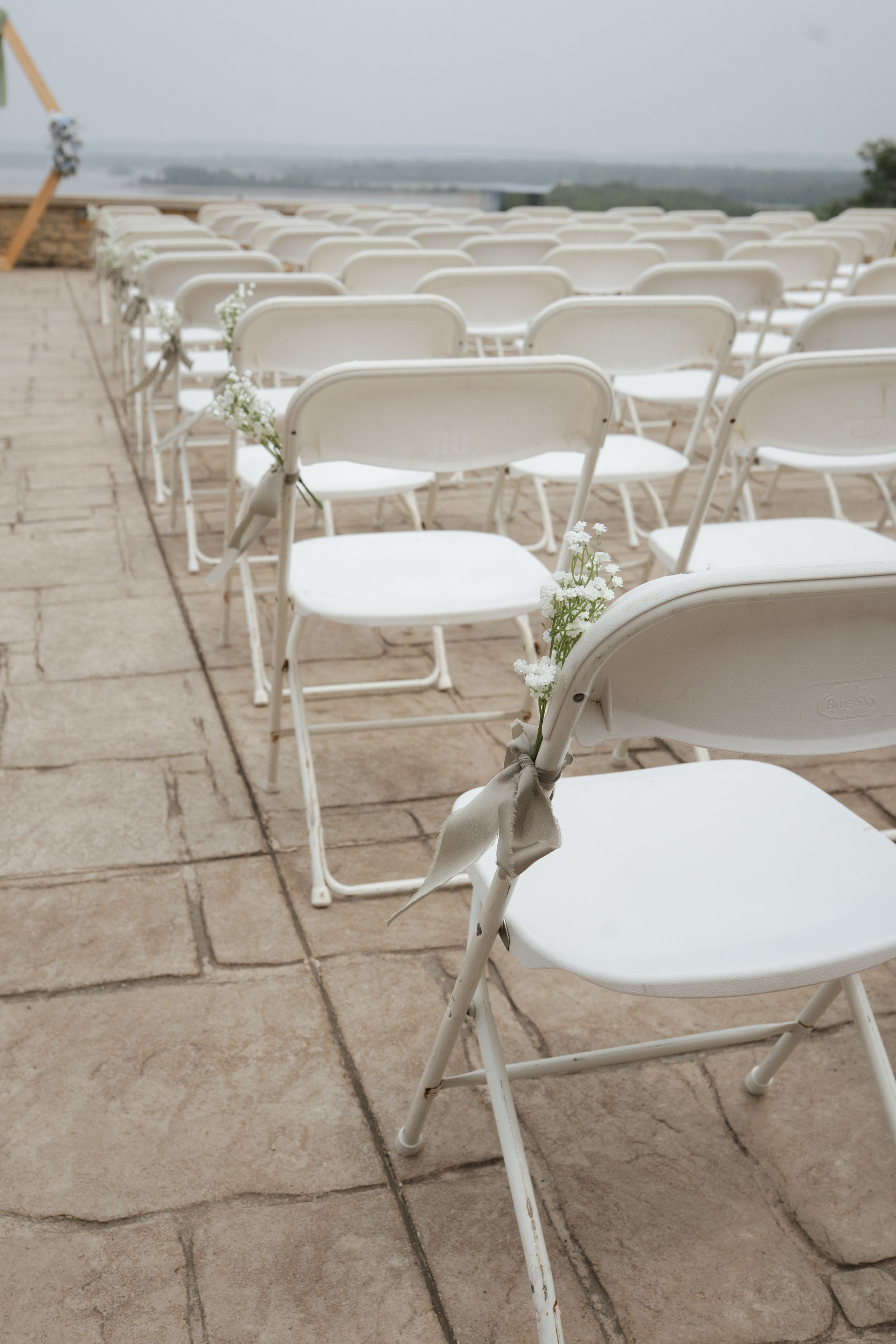 Rows of white folding chairs set up for an outdoor ceremony on a stone patio.