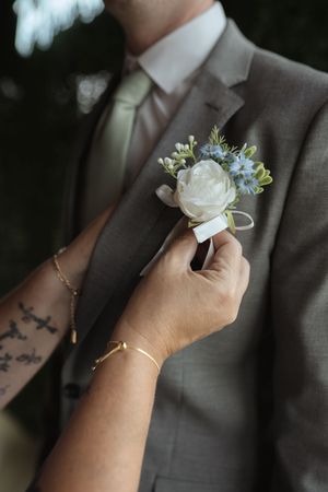 Close-up of hands pinning a white rose boutonniere on a gray suit lapel.