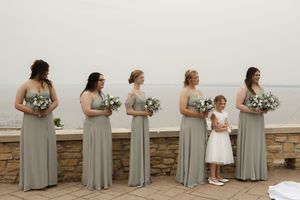 Bridesmaids in sage green dresses pose in a line against a white wall.