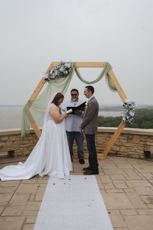 Wedding ceremony under a wooden hexagonal arch with sage green draping and floral decorations.
