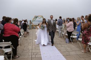 Wedding ceremony recessional on a stone patio with guests seated on white chairs.