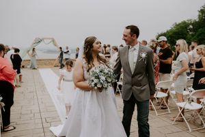 Wedding guests celebrate during an outdoor ceremony on a stone patio with white folding chairs.